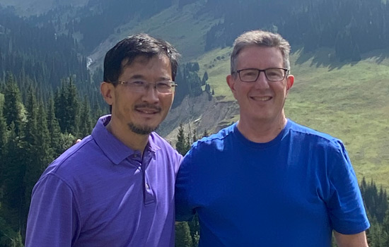 Two men stand together outdoore in the mountains